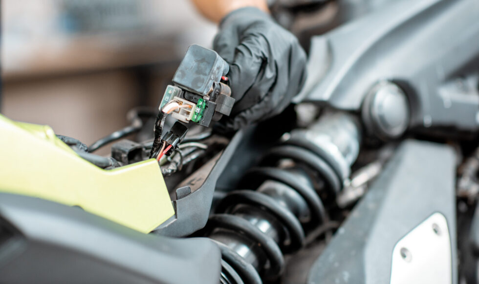 Electrician repairing motorcycle wiring Electrician or repairman in protective gloves connecting wiring in the motorcycle during a repairment at the workshop, close-up